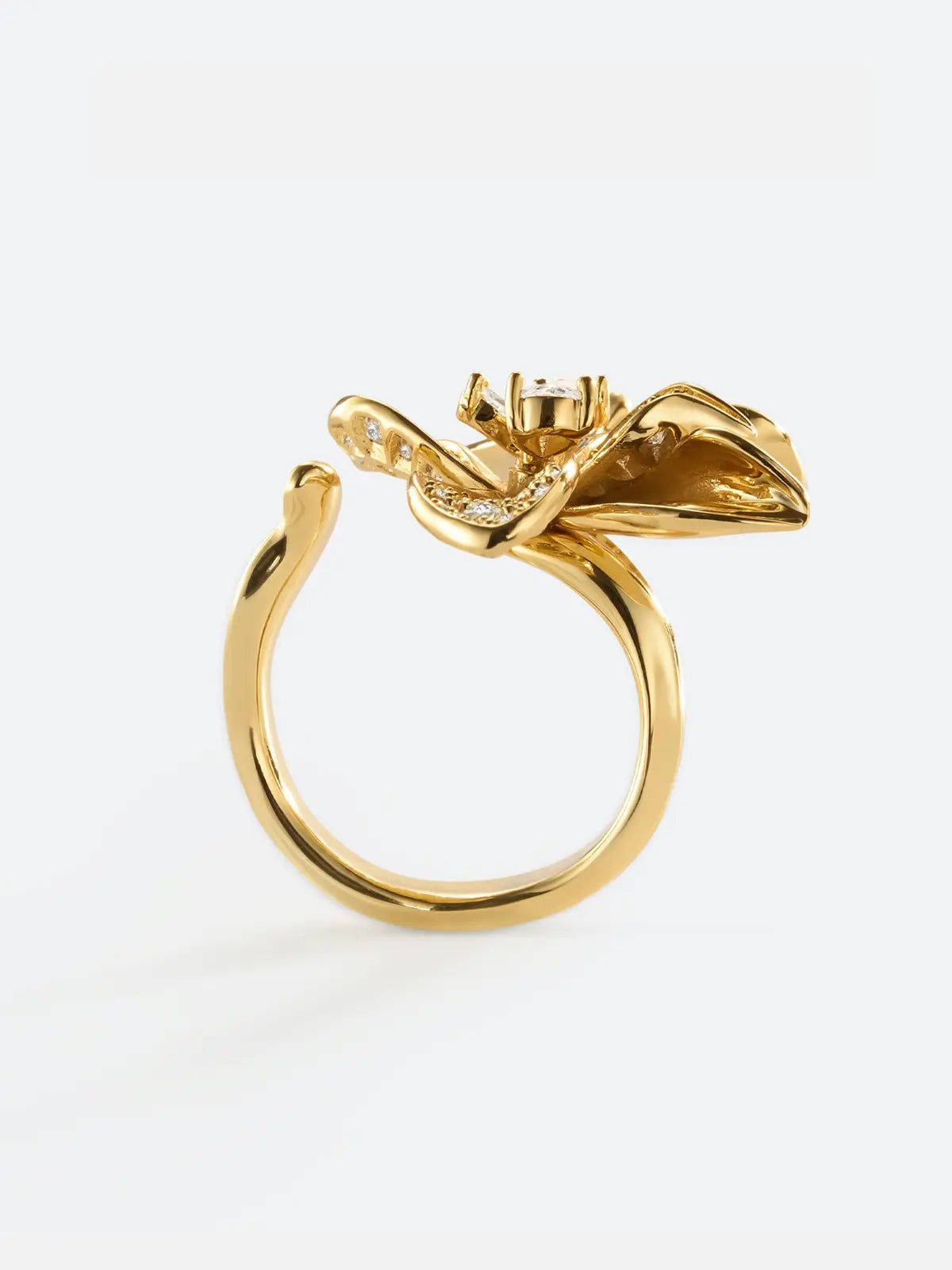 Tactilery Blossom Ring displayed at an angle on a white background showing the three-dimensional depth of the oversized gold five-petal orchid flower cocktail ring with pavé zircon upper petals, smooth gold lower petals, and wide tapered gold band