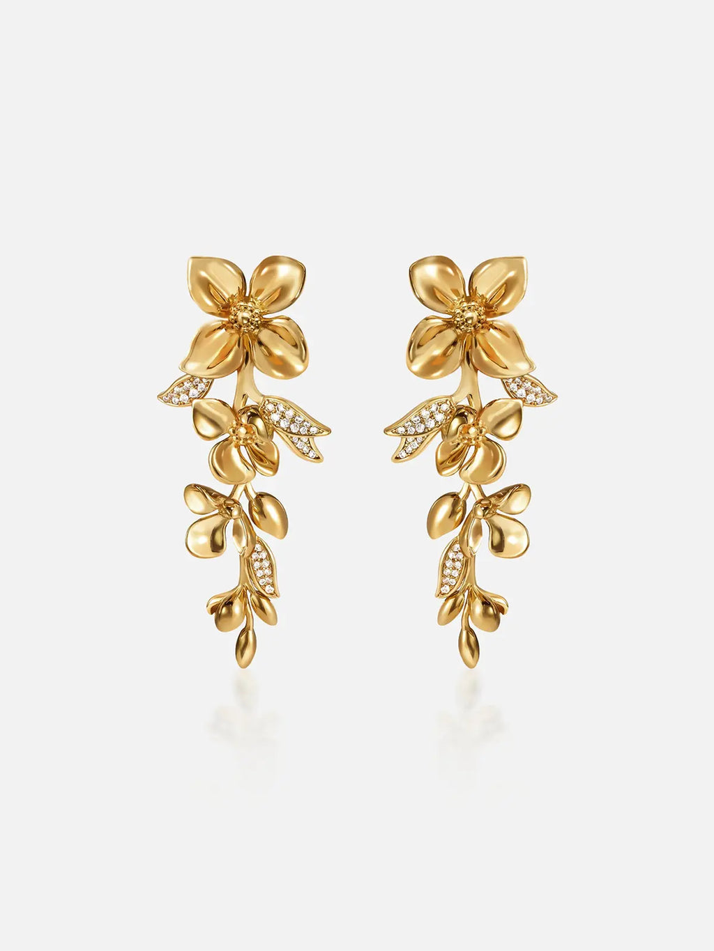 Pair of Tactilery Tassel Detachable Drop Earrings in polished gold on a light grey background, the long cascading drop composed of a large five-petal blossom flower stud top with smooth domed petals and pavé zircon stamens, a detachable lower section with a smaller five-petal blossom flower and a trailing spray of polished gold oval leaf buds with pavé zircon leaf accents, shown assembled as a full drop