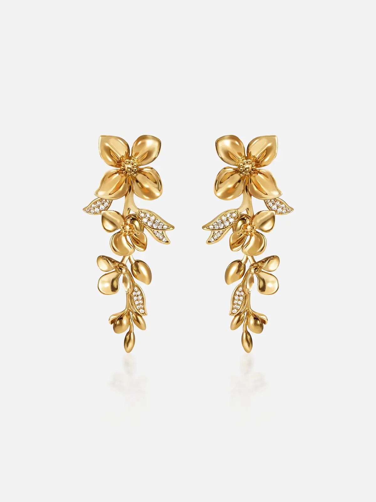 Pair of Tactilery Tassel Detachable Drop Earrings in polished gold on a light grey background, the long cascading drop composed of a large five-petal blossom flower stud top with smooth domed petals and pavé zircon stamens, a detachable lower section with a smaller five-petal blossom flower and a trailing spray of polished gold oval leaf buds with pavé zircon leaf accents, shown assembled as a full drop