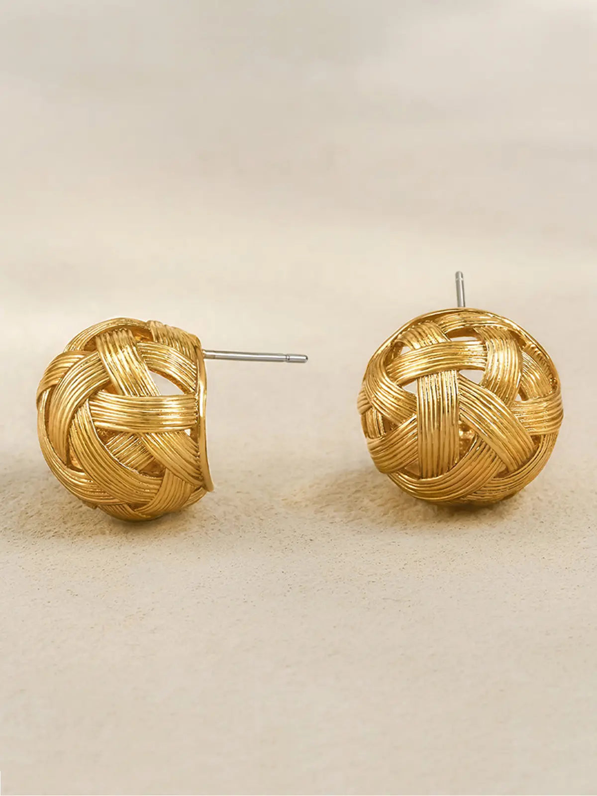Pair of Tactilery Brushed Woven Gold Ball Stud Earrings in matte brushed gold on a warm sand surface