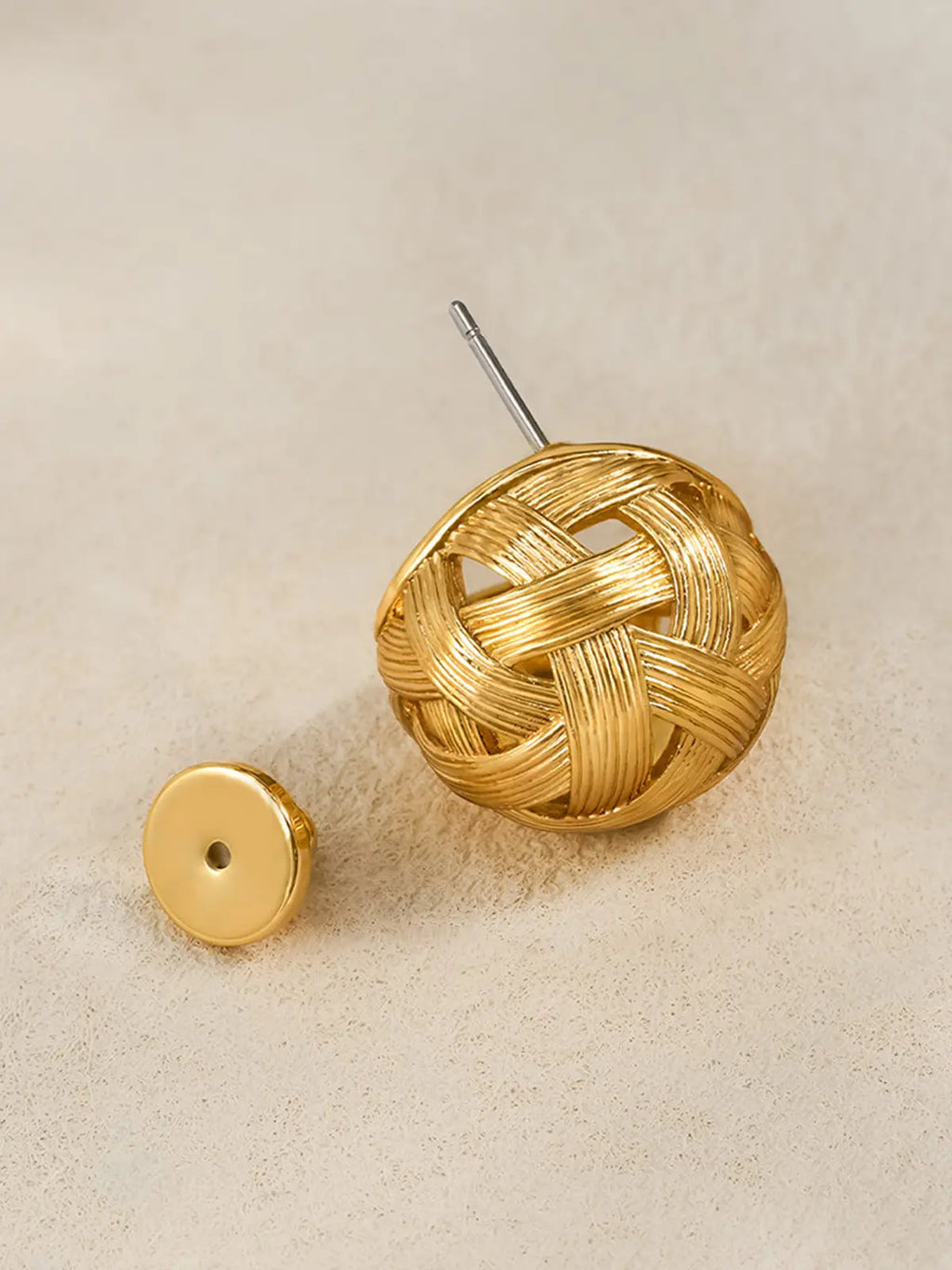 Single Tactilery Brushed Woven Gold Ball Stud Earring in matte brushed gold on a warm sand surface with the gold disc butterfly back removed and placed beside it