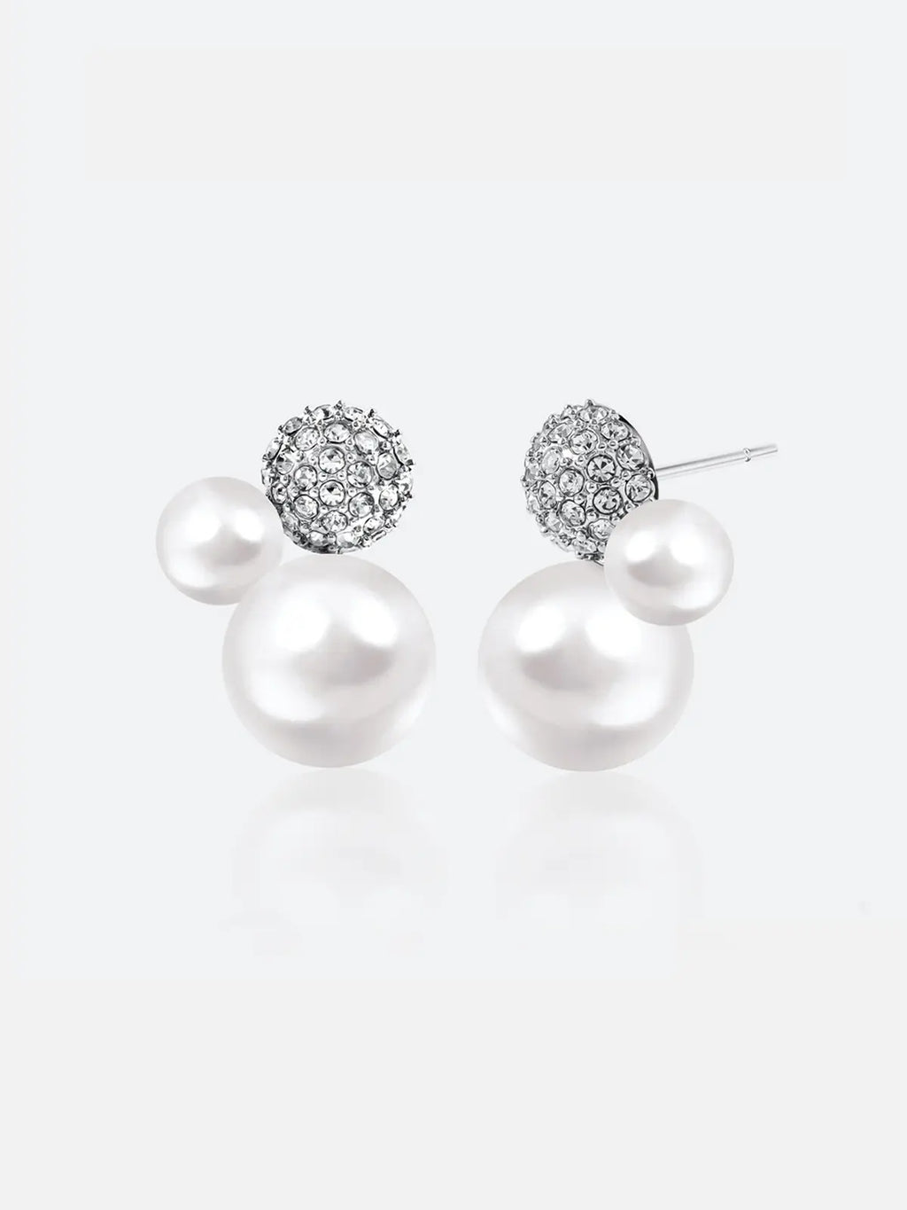 Pair of Tactilery Bubble Stud Earrings in silver on a light grey background, the cluster stud with a fully pavé zircon dome sphere at top, a small white pearl sphere at mid-right, and a large white pearl sphere at bottom, with silver post pins