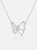 A Tactilery butterfly wing necklace with a milky white inlay, set against a light gray background with a soft reflection below.
