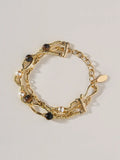 A Tactilery caramel tiger eye multi layer bracelet featuring chain links, rope textures, faux pearls, dark brown beads, and a small oval gold tag, displayed on a light gray background.