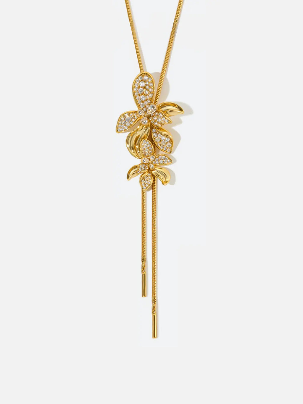 Tactilery Flower Narrative Long Necklace in matte brushed gold on a white background, the long Y-drop necklace with a fine polished gold satellite chain suspending a cluster of five sculptural matte brushed gold elements — three dimensional five-petal flower blossoms, small leaf sprigs, and scattered prong-set round zircon accents — gathered at the drop point, with a fine polished gold cable chain extension and lobster clasp