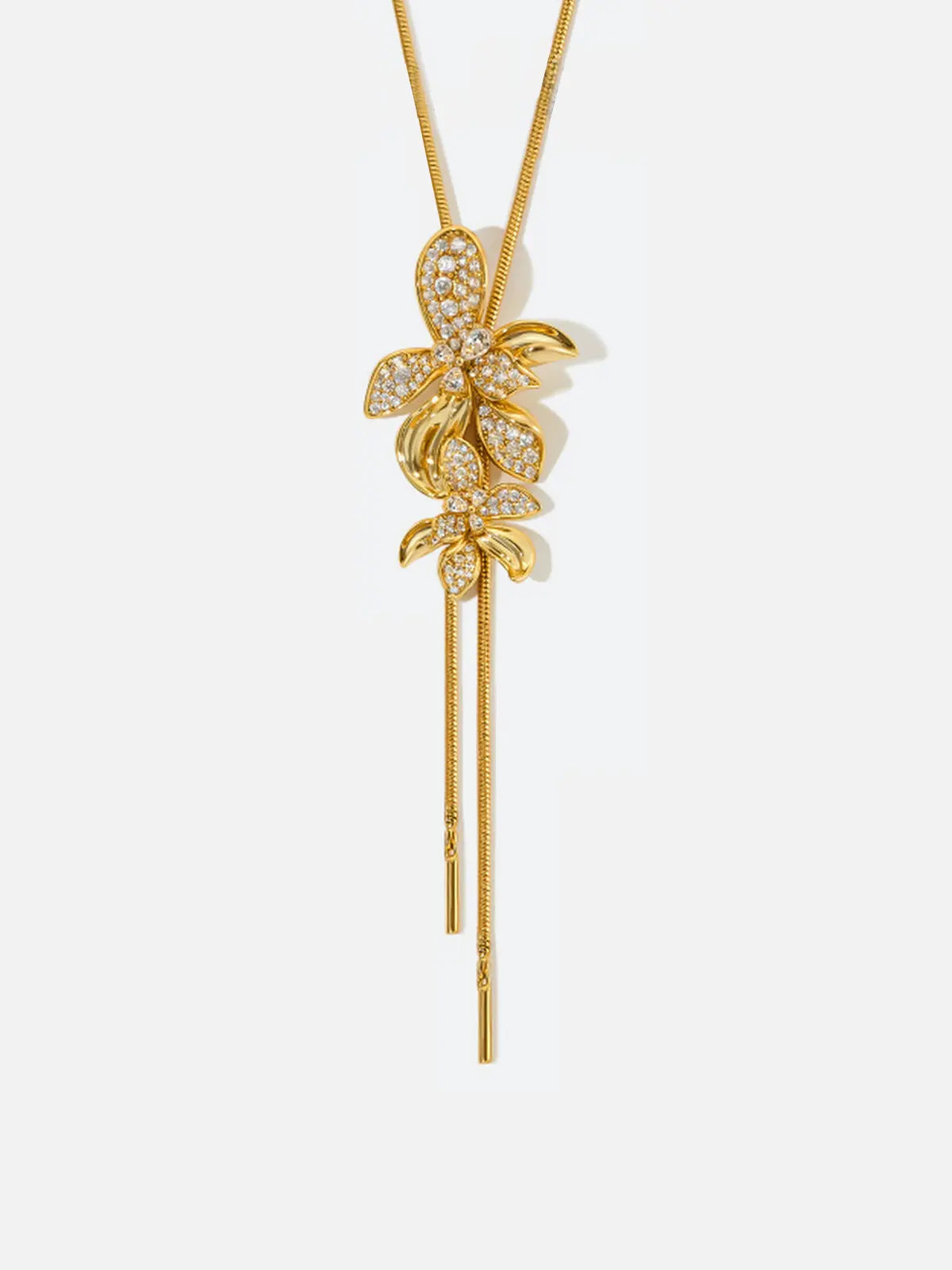 Tactilery Flower Narrative Long Necklace in matte brushed gold on a white background, the long Y-drop necklace with a fine polished gold satellite chain suspending a cluster of five sculptural matte brushed gold elements — three dimensional five-petal flower blossoms, small leaf sprigs, and scattered prong-set round zircon accents — gathered at the drop point, with a fine polished gold cable chain extension and lobster clasp