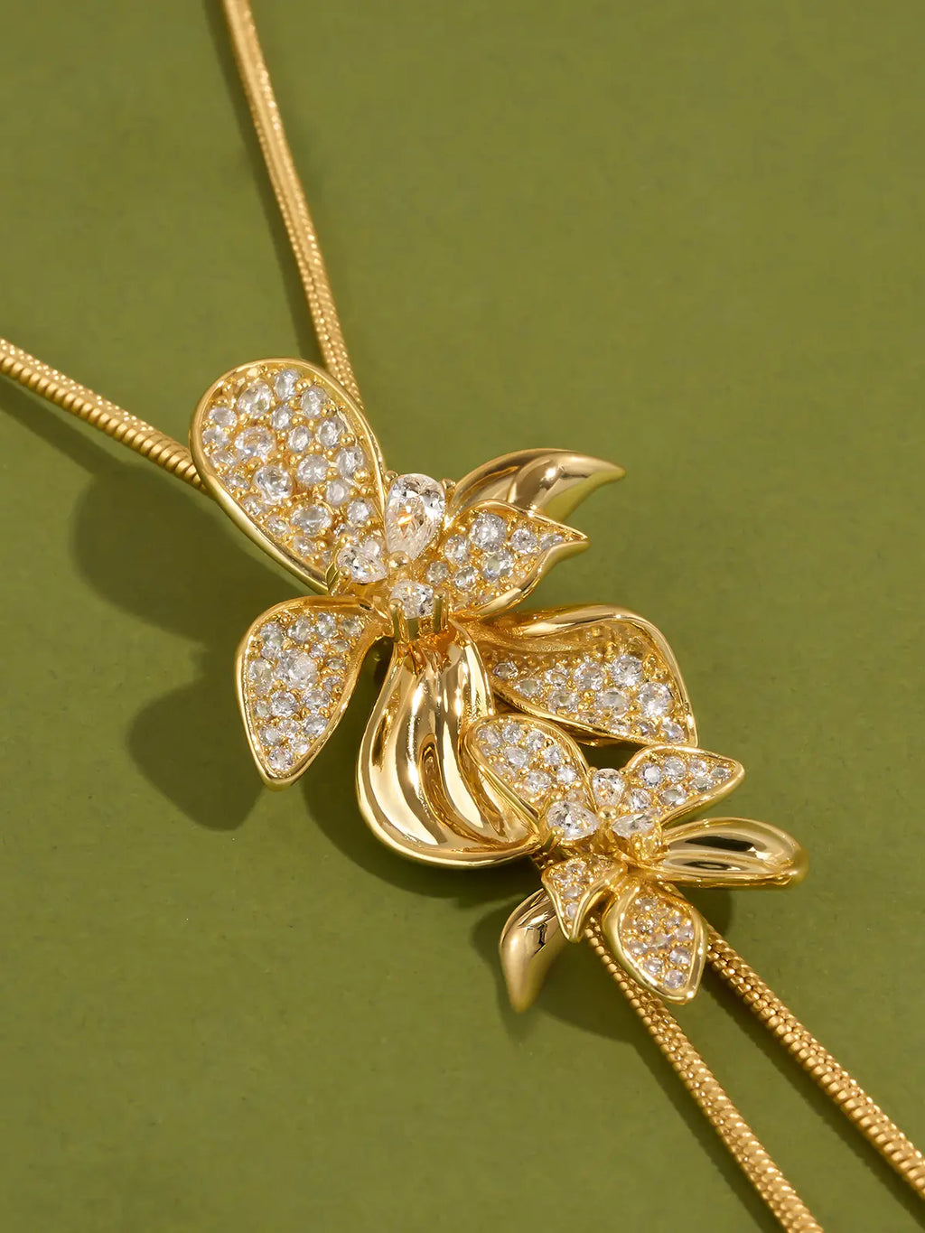 Tactilery Flower Narrative Long Necklace in matte brushed gold displayed laid out flat on a white background showing the full necklace length, the fine polished gold satellite chain extending the full length with the lobster clasp and extension chain at top and the sculptural matte brushed gold flower blossom and leaf cluster with prong-set round zircon accents at the bottom drop point