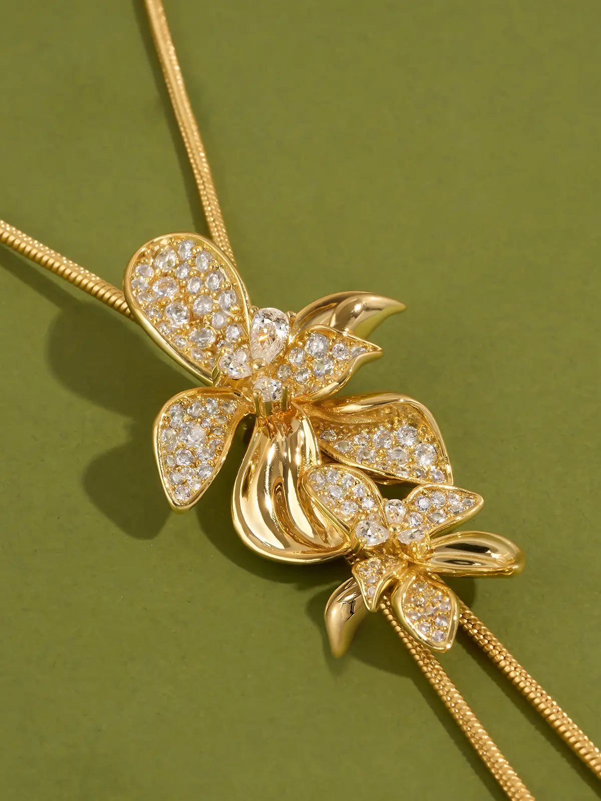 Tactilery Flower Narrative Long Necklace in matte brushed gold displayed laid out flat on a white background showing the full necklace length, the fine polished gold satellite chain extending the full length with the lobster clasp and extension chain at top and the sculptural matte brushed gold flower blossom and leaf cluster with prong-set round zircon accents at the bottom drop point