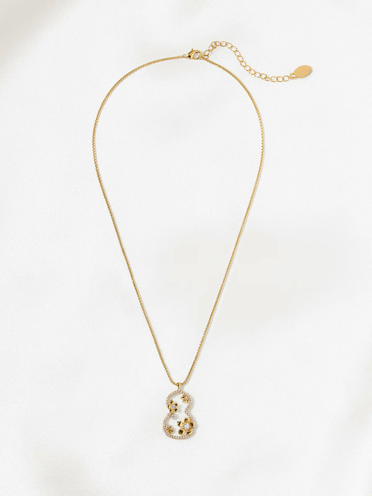 Tactilery Dream Gourd Window Necklace in matte brushed gold displayed laid out flat on a white surface showing the full necklace length, the fine polished gold box chain extending the full length with the lobster clasp and oval tag charm extension chain at top and the large open-frame double-gourd silhouette pendant with pavé zircon inner border and sculptural interior garden scene at bottom