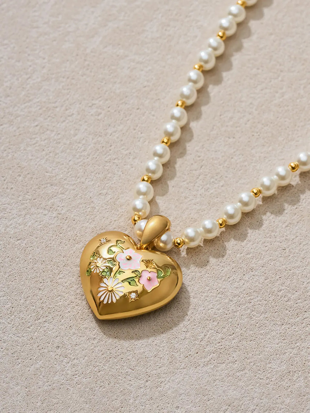 Flat-lay detail of the Tactilery Garden Floral Pearl Necklace on a warm cream surface, the sculptural polished gold five-petal sunburst flower pendant with prong-set round zircon shown alongside the graduated freshwater pearl strand and small polished gold seed bead spacers, the graduating pearl size and bead pattern clearly visible