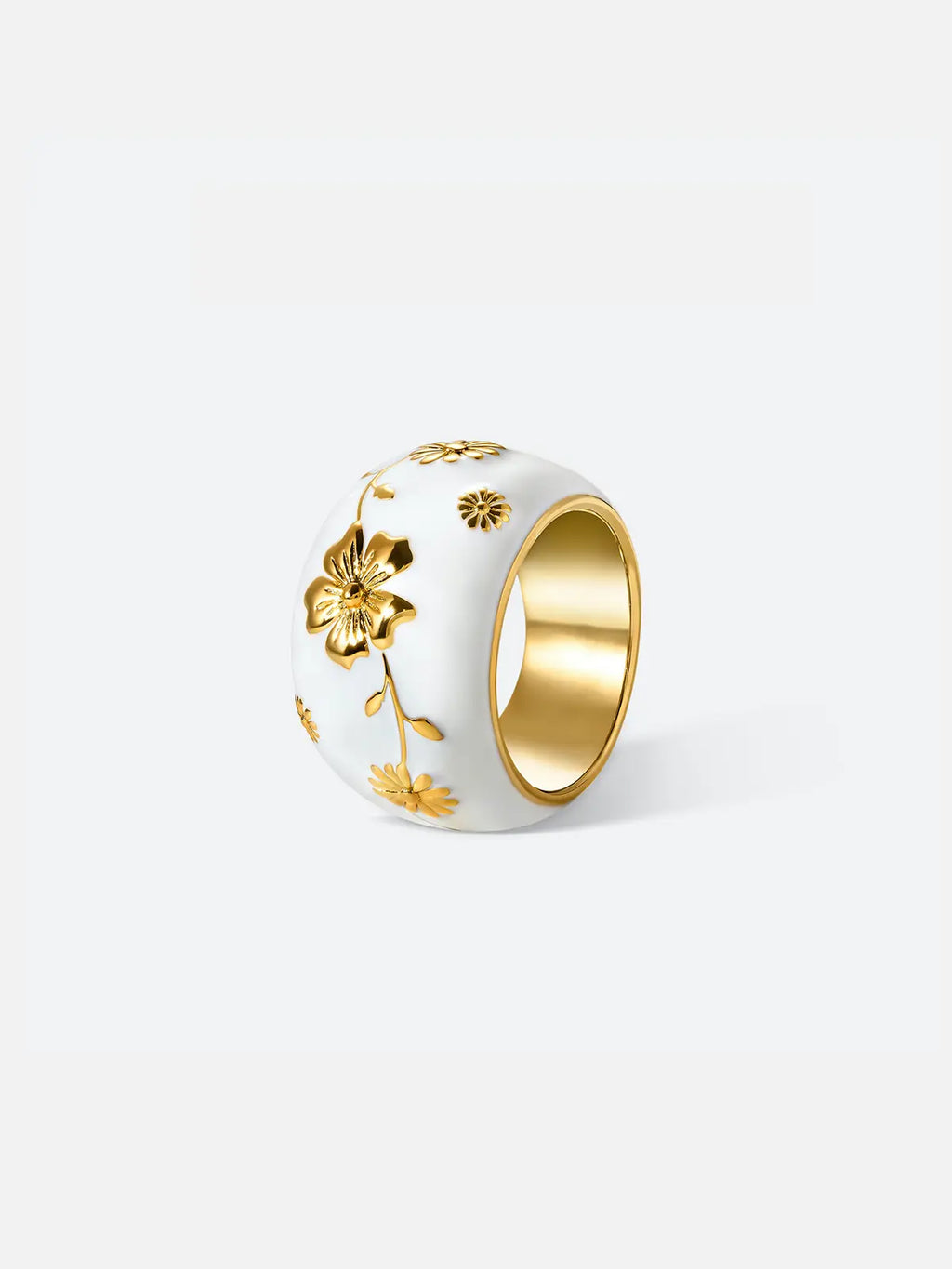 Tactilery Garden Relief Floral Ring displayed upright on a warm beige linen surface, the wide white enamel dome band with raised gold botanical vine, daisy blooms, and leaf motifs wrapping around the band, with polished gold interior visible at top