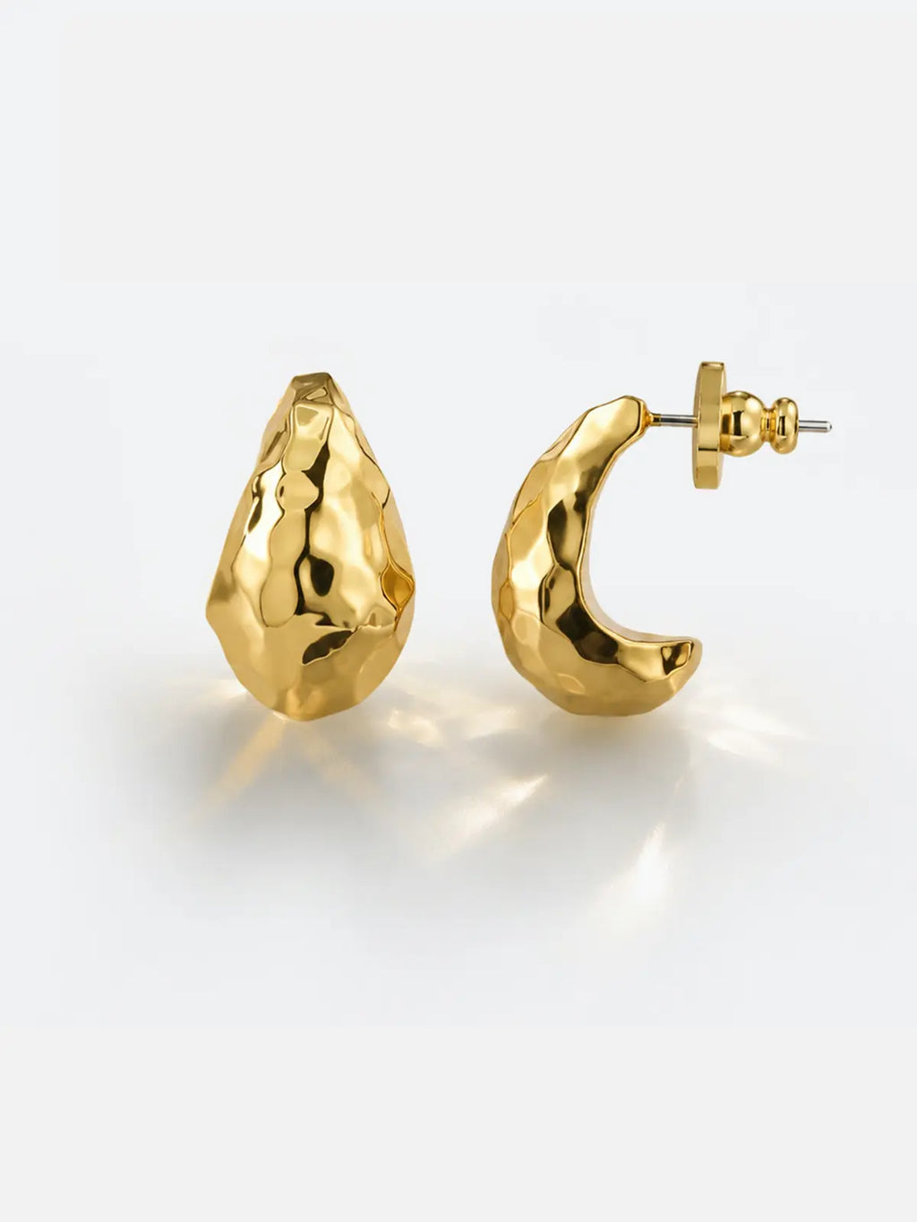 Pair of Tactilery Hammered Teardrop Earrings in polished gold on a white background, one shown face-on as a chunky teardrop stud and one shown in C-hoop profile, the wide chunky polished gold C-hoop with an irregular hammered faceted surface creating a molten sculptural texture, with gold ball screw-back fitting and silver post pin