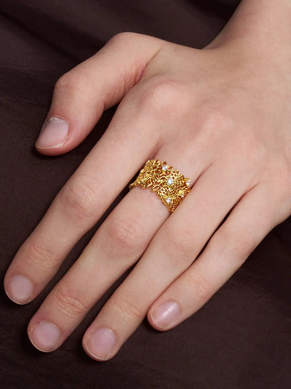 Close-up of a model's hand wearing the Tactilery Lace Garden Open Ring, showing the full width of the gold openwork lace floral cuff band with intricate vine and flower lattice pattern and five prong-set round zircon accents across the surface