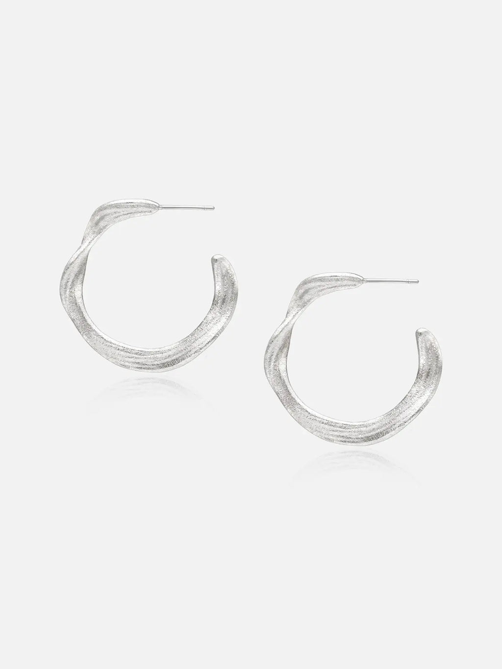 Pair of Tactilery Lake Ripple Hoop Earrings in matte brushed silver on a white background, the large organic C-hoop with a gently undulating wavy silhouette and fine horizontal brushed ripple texture across the wide flat band surface, with silver post pin at top