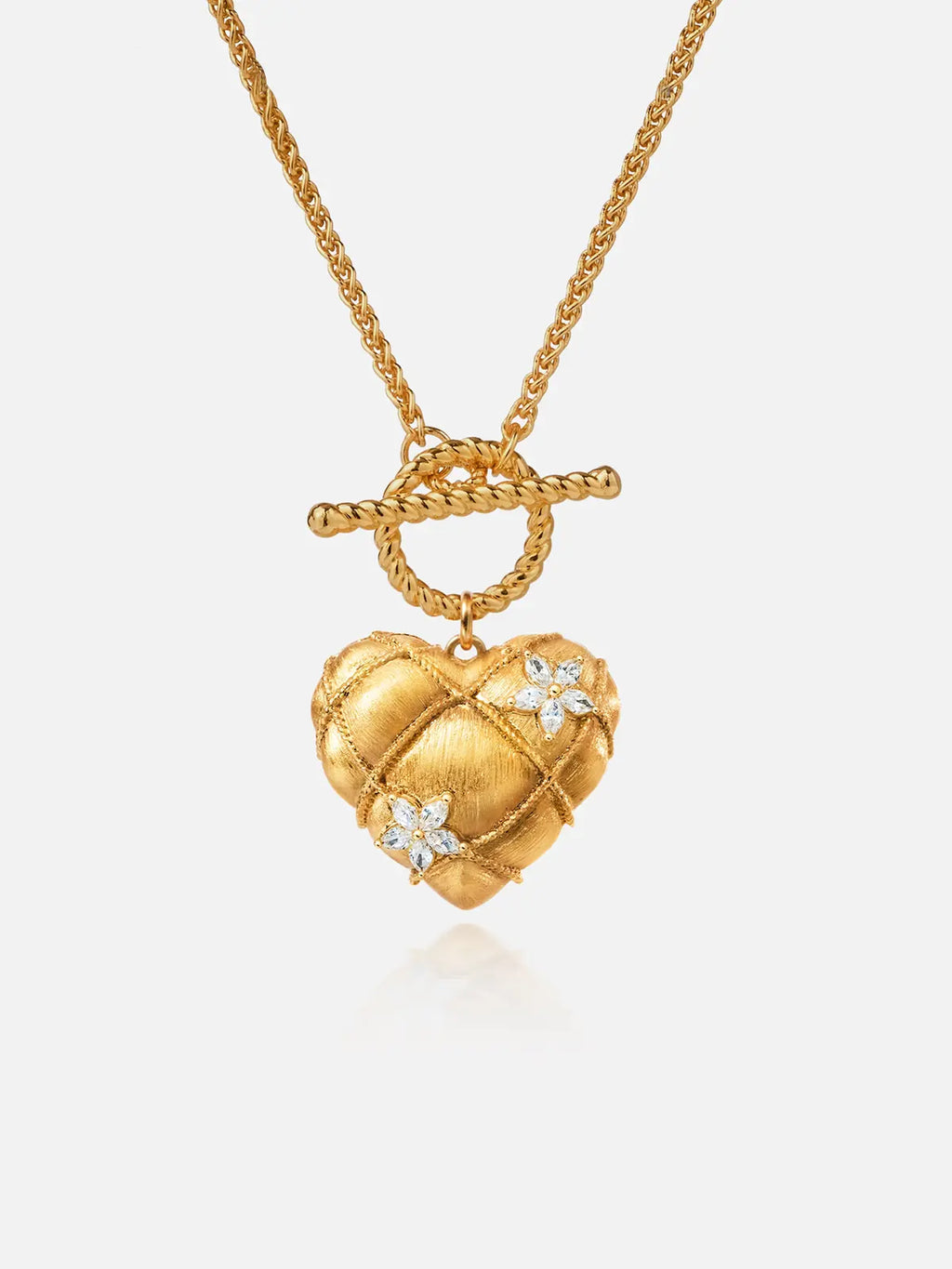 Tactilery Love Blossom Necklace in matte brushed gold on a white background, the large three-dimensional puffy heart pendant with a matte brushed gold quilted diamond-grid surface edged by fine twisted gold rope milgrain borders at each grid line, two prong-set four-petal marquise zircon blossom flower accents scattered across the face, suspended from a twisted gold rope OT toggle ring by a jump ring, on a fine polished gold wheat chain with a twisted gold rope OT toggle bar clasp