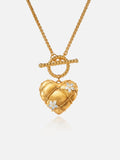 Tactilery Love Blossom Necklace in matte brushed gold on a white background, the large three-dimensional puffy heart pendant with a matte brushed gold quilted diamond-grid surface edged by fine twisted gold rope milgrain borders at each grid line, two prong-set four-petal marquise zircon blossom flower accents scattered across the face, suspended from a twisted gold rope OT toggle ring by a jump ring, on a fine polished gold wheat chain with a twisted gold rope OT toggle bar clasp