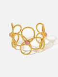 Tactilery Openwork Flower Cuff Bracelet in matte sand-textured gold on a white background, the wide open cuff constructed from interlocking looped gold wire forming three overlapping five-petal flower outlines across the band, each flower center accented with a small bezel-set round pink rose quartz cabochon, the open C-cuff silhouette showing the full sculptural wire lattice construction