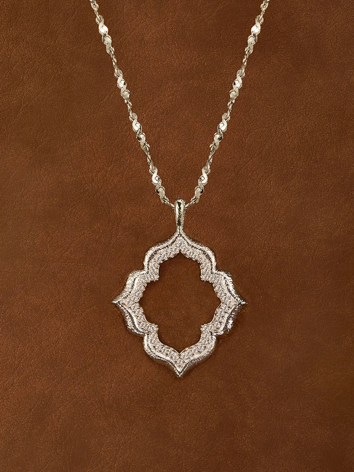 Tactilery Persimmon Calyx Openwork Necklace in polished gold displayed laid out flat on a white surface showing the full necklace length, the fine polished gold twisted petal-link chain extending the full length with the lobster clasp and oval tag charm extension chain at top and the large open-frame four-lobe persimmon calyx flower pendant at bottom