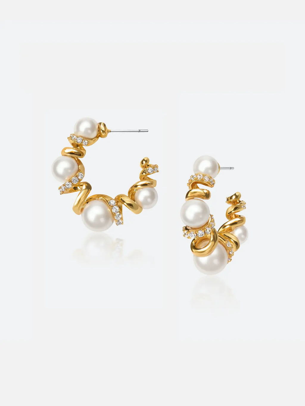 Pair of Tactilery Spiral Twist Pearl Hoop Earrings in polished gold on a light grey background, the large C-hoop constructed from a continuous polished gold spiral twist wire interspersed with five graduated white pearl spheres — small at top, progressively larger toward the bottom — with pavé zircon bar accents at each spiral junction, with silver post pins at top