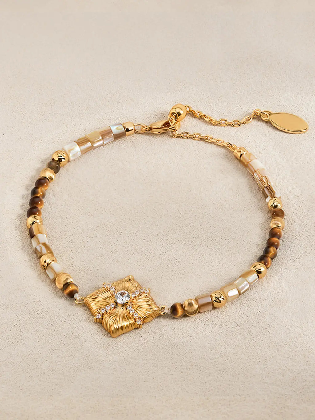 A Tactilery sugar cube beaded bracelet featuring a textured floral centerpiece with a clear rhinestone, alternating with brown and cream beads, displayed on a neutral beige background.