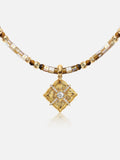 A Tactilery sugar cube beaded necklace featuring a central diamond-shaped pendant with a clear central stone and surrounding gold rays, accented by brown and metallic gold beads on a light gray background.