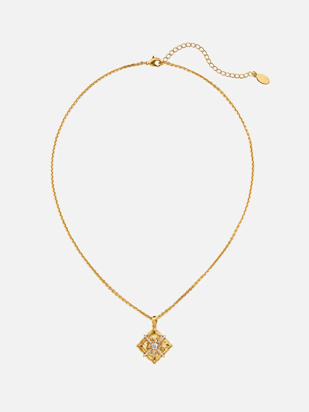Tactilery Sugar Cube Necklace in polished gold displayed at a three-quarter angle on a warm cream surface, the square diamond-shaped pendant with four deeply radiating sunburst line-engraved petal-like lobes, central prong-set large round zircon, and pavé zircon cross accent shown in detail, with the fine polished gold cable chain and bail visible above