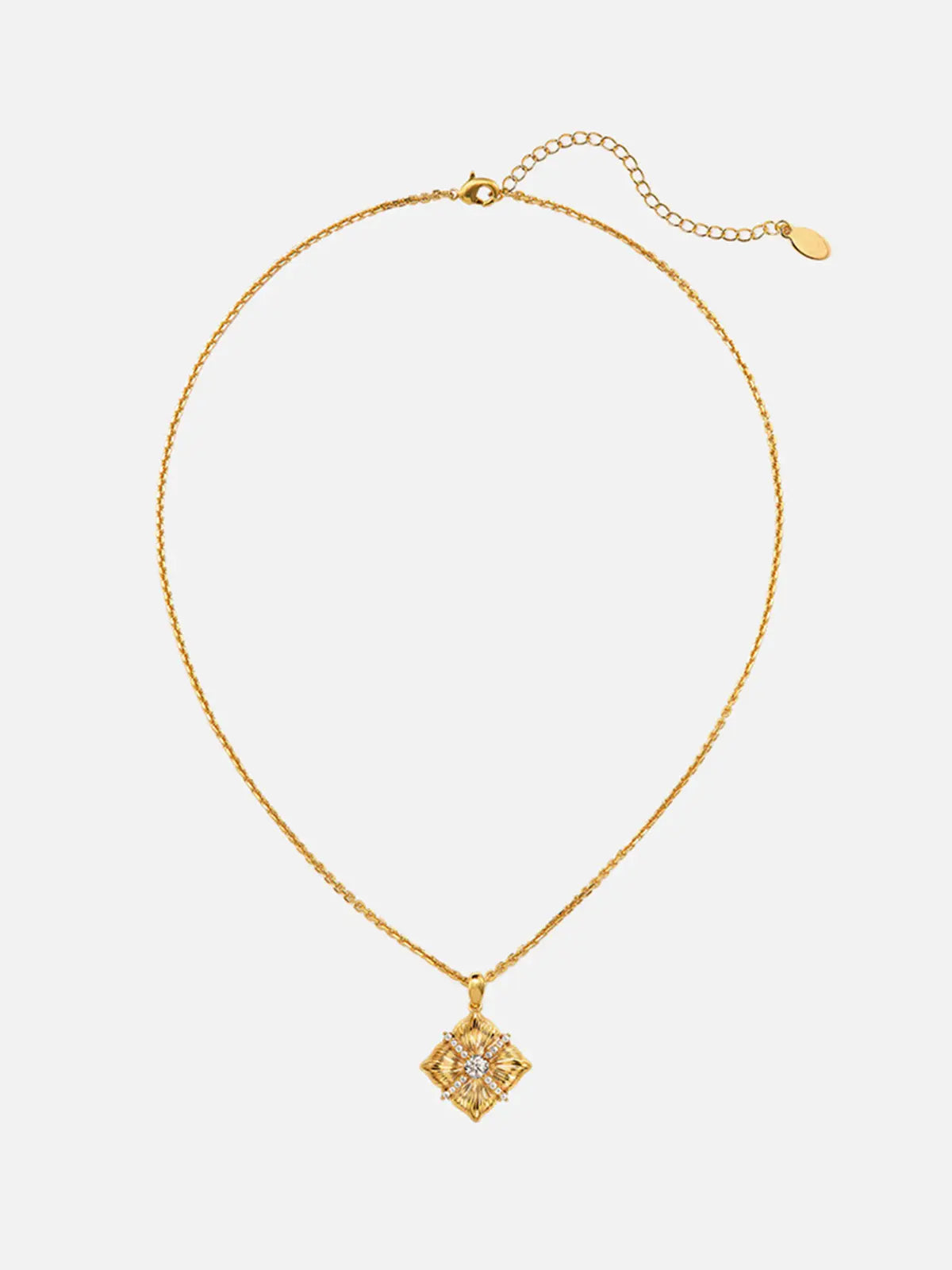Tactilery Sugar Cube Necklace in polished gold displayed at a three-quarter angle on a warm cream surface, the square diamond-shaped pendant with four deeply radiating sunburst line-engraved petal-like lobes, central prong-set large round zircon, and pavé zircon cross accent shown in detail, with the fine polished gold cable chain and bail visible above
