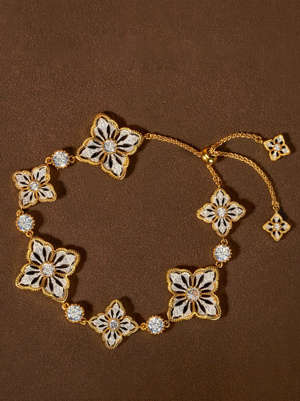 A gold-toned floral two tone persimmon calyx bracelet with white enamel-style inlays and clear rhinestone accents, arranged on a textured brown background.