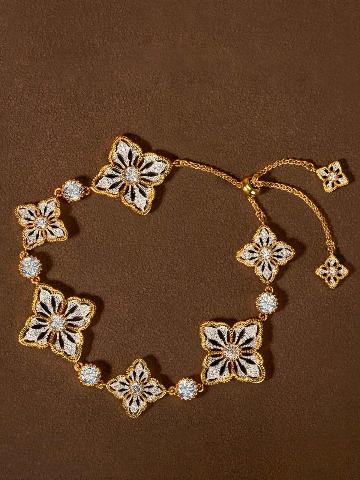 A gold-toned floral two tone persimmon calyx bracelet with white enamel-style inlays and clear rhinestone accents, arranged on a textured brown background.
