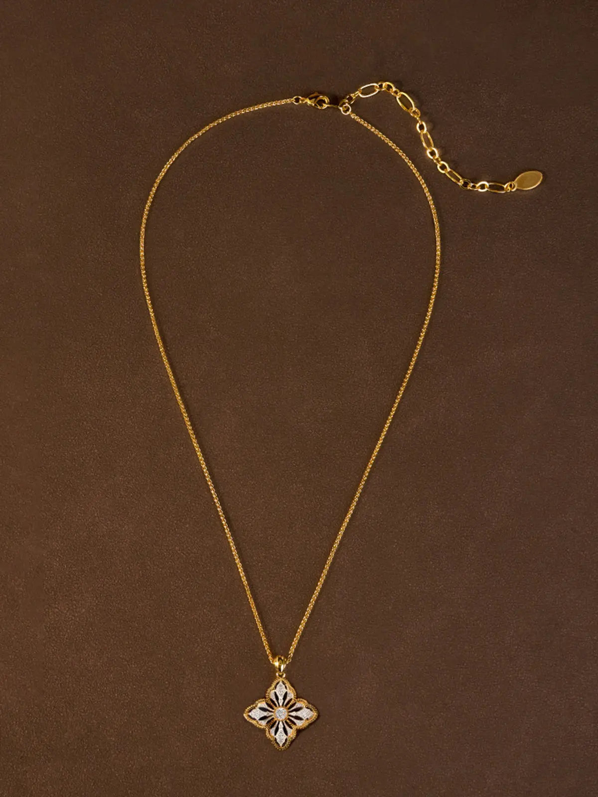 Extreme close-up of the Tactilery Two-Tone Persimmon Calyx Necklace pendant on a warm cream surface, the large two-tone four-petal persimmon calyx flower with matte brushed silver openwork petal body, fine polished gold milgrain rope border, and central prong-set large round zircon in sharp detail, with the polished gold twisted rope chain bail visible above