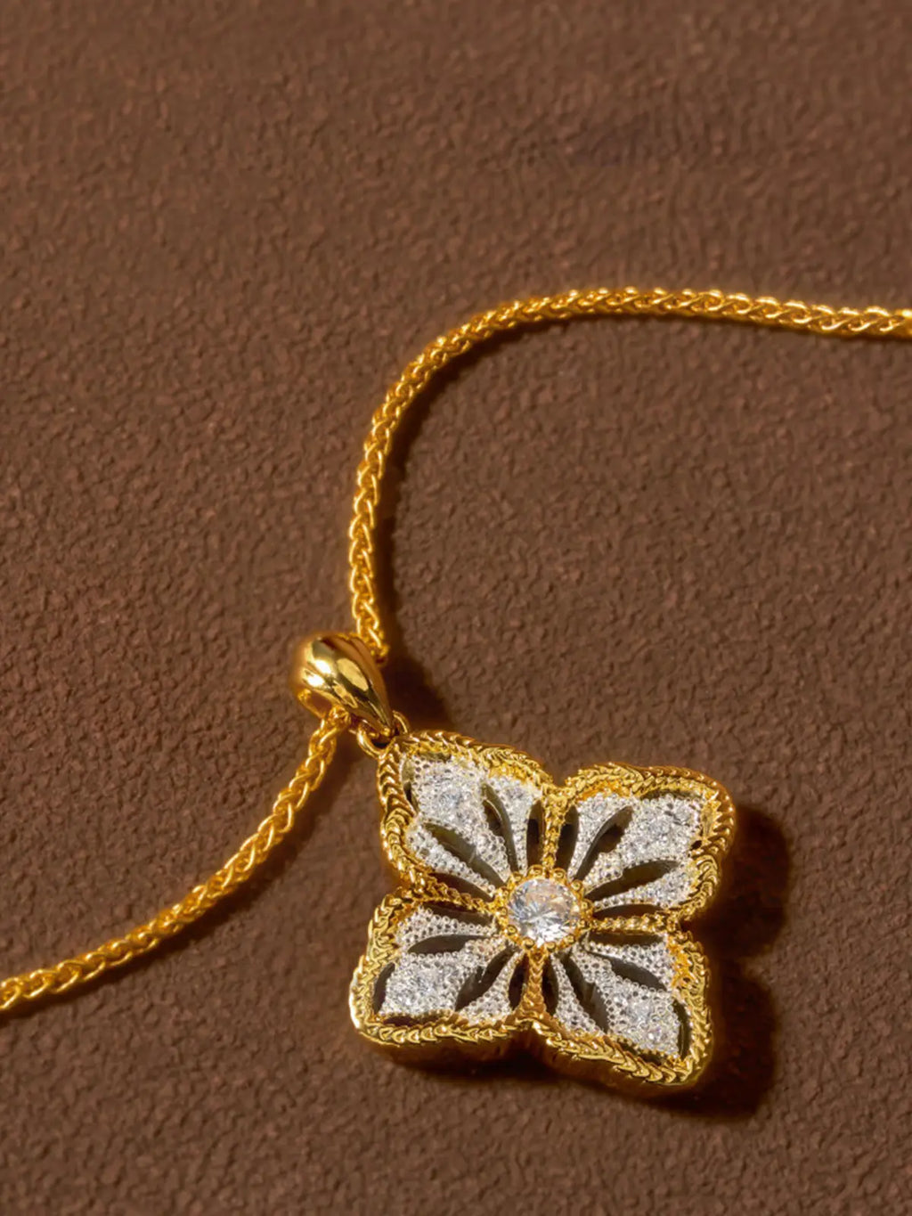 Tactilery Two-Tone Persimmon Calyx Necklace in polished gold and matte brushed silver displayed on a warm cream surface showing the back of the pendant, the smooth matte brushed silver back face of the four-petal persimmon calyx flower with the fine polished gold milgrain rope border edge visible, and the polished gold twisted rope chain bail at top