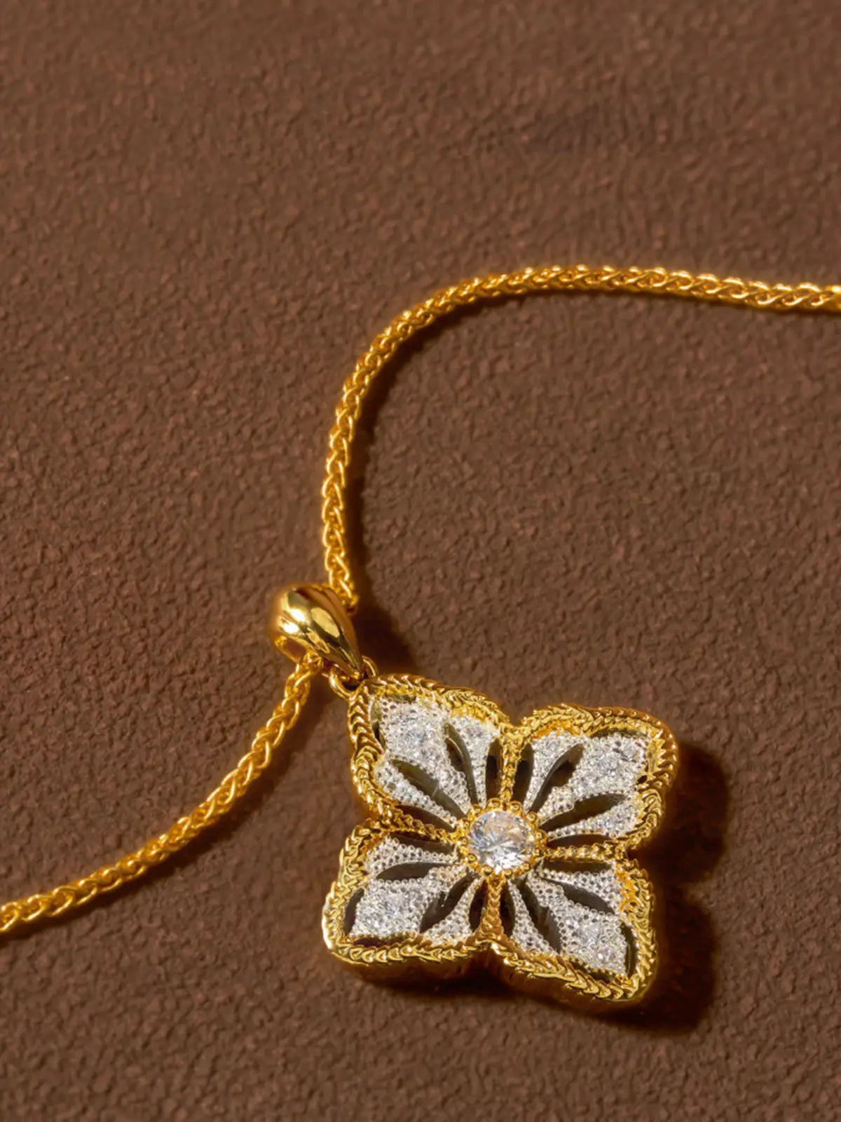 Tactilery Two-Tone Persimmon Calyx Necklace in polished gold and matte brushed silver displayed on a warm cream surface showing the back of the pendant, the smooth matte brushed silver back face of the four-petal persimmon calyx flower with the fine polished gold milgrain rope border edge visible, and the polished gold twisted rope chain bail at top